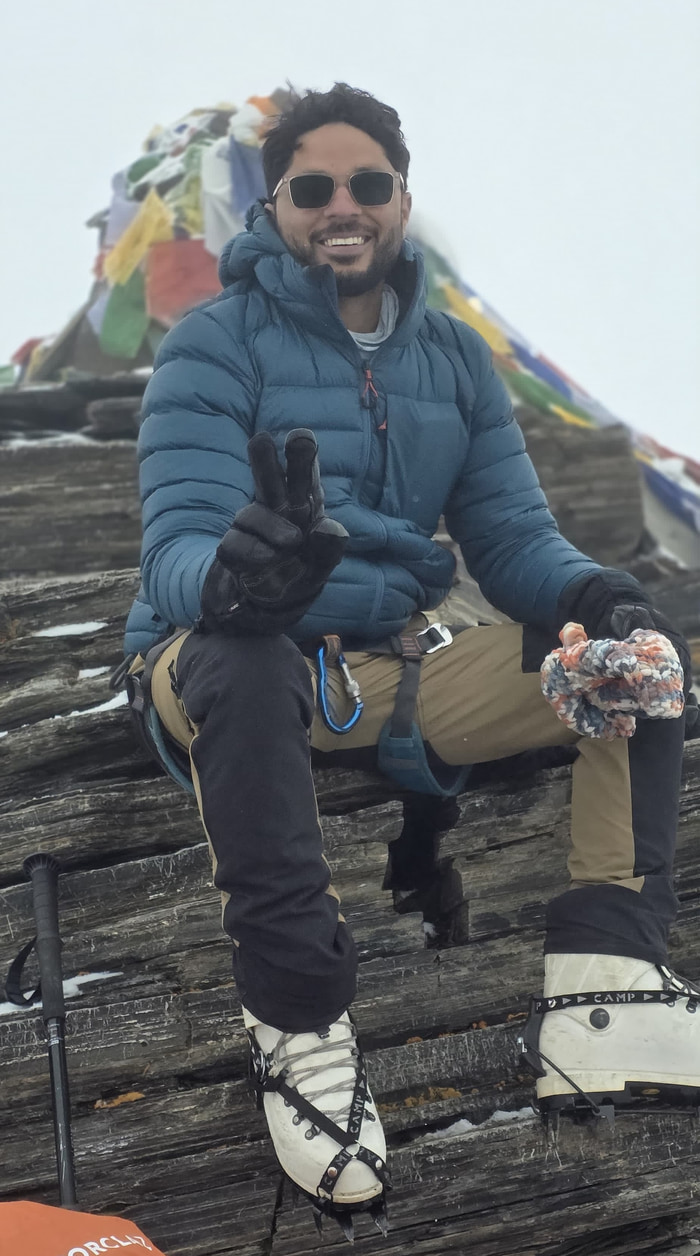 Sitting at the summit in crampons and a blue down jacket.